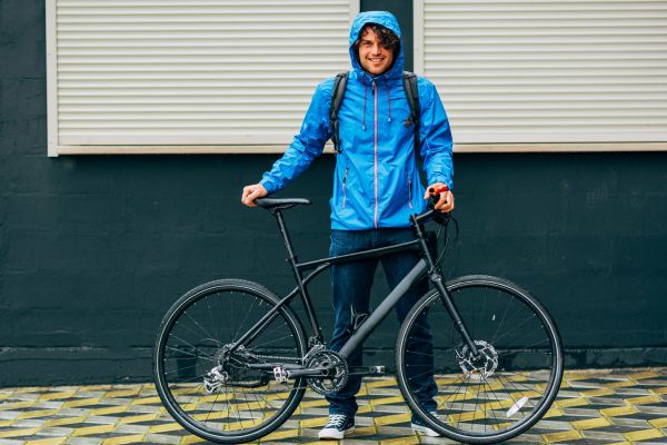 A young man stands with his bike in a blue rain jacket.